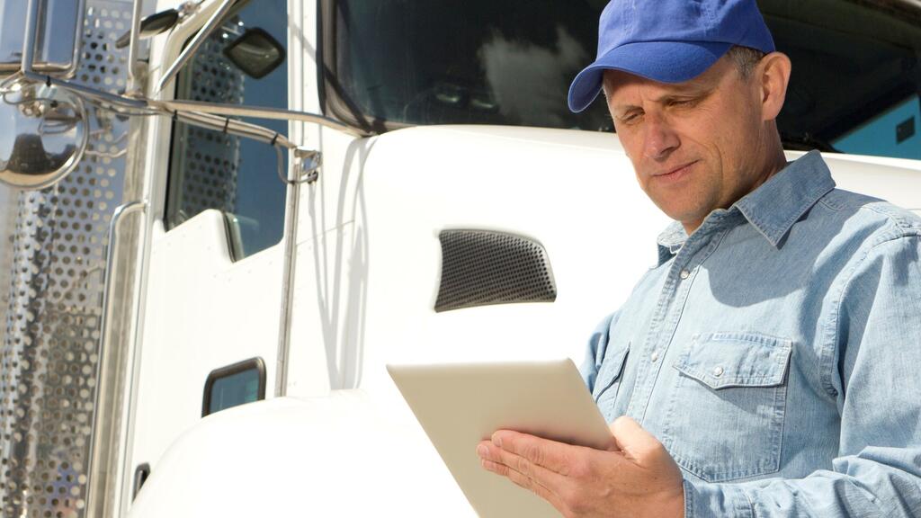 truck driver in front of truck holding tablet